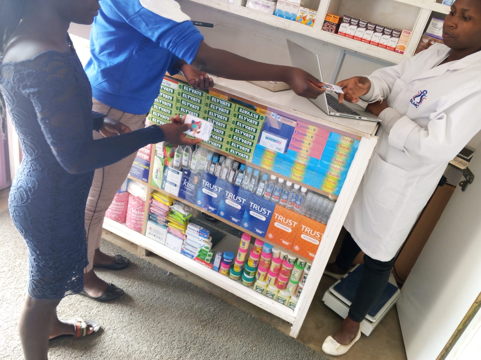 A young person presenting a Wellness Card to an SLMC nurse beside a clinic laptop